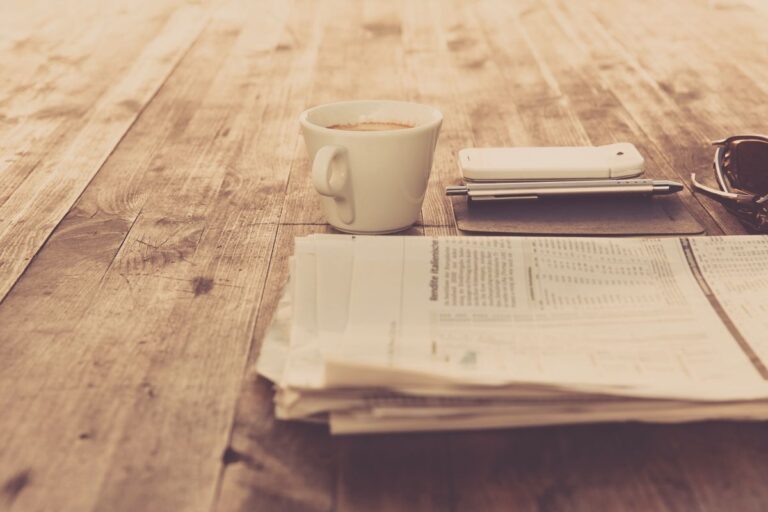 Coffee cup beside a newspaper on wood